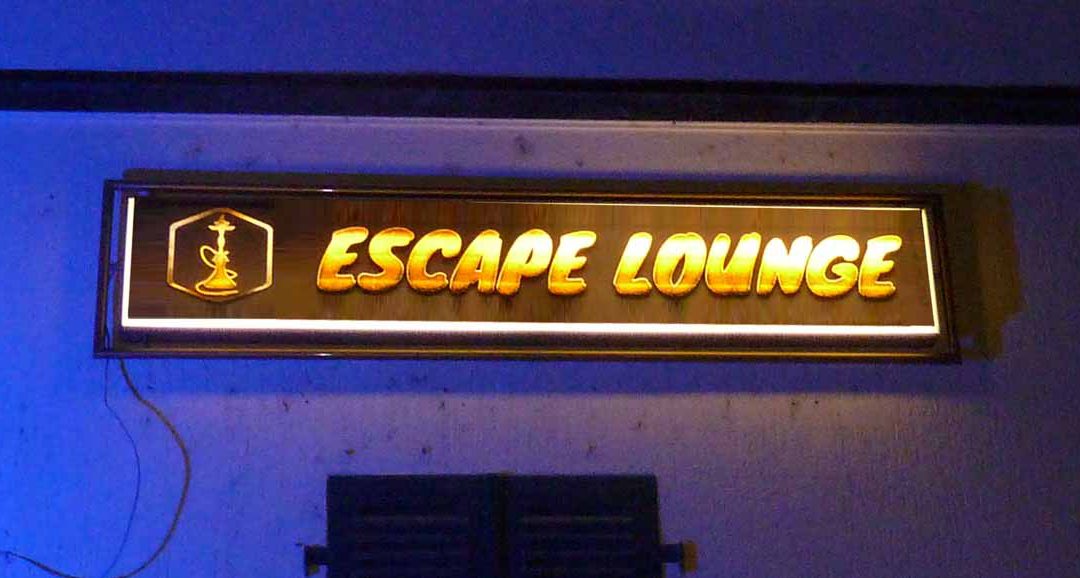 Neue Klebefolie, die von hinten durchleuchtet wird auf altem Leuchtkasten mit dem Text "Escape Lounge" und der Abbildung einer Shisha